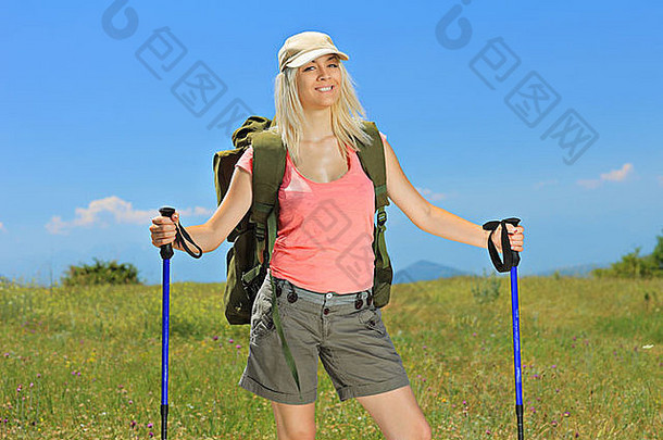 一个微笑的女人拿着背包和<strong>登山杖</strong>在户外摆姿势