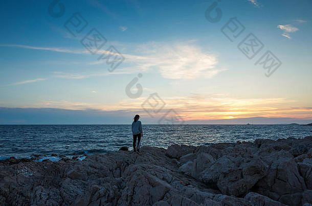克罗地亚亚得里亚海附近的日落时分，一名年轻女子站在户外。黄昏时分，达尔马提亚的海洋呈现出美丽的自然和风景。女孩h