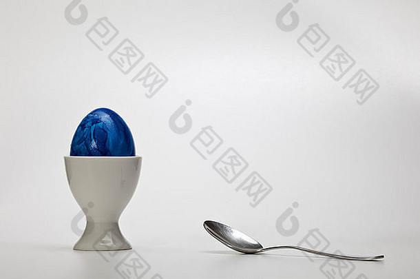 一个复活节彩蛋，放在一个带金属勺子的瓷质蛋杯里