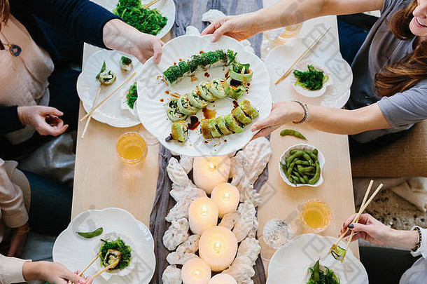 俯瞰图：四个人共享一顿饭、几盘寿司和一张桌子，准备庆祝晚宴。