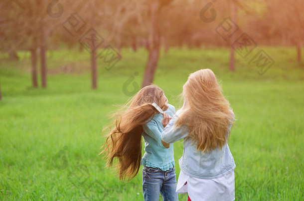 两个美丽的棕色头发和金色头发的小女孩在公园的户外用发刷梳头