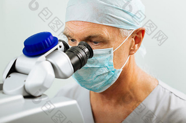 成熟的医生坐着前面显微镜