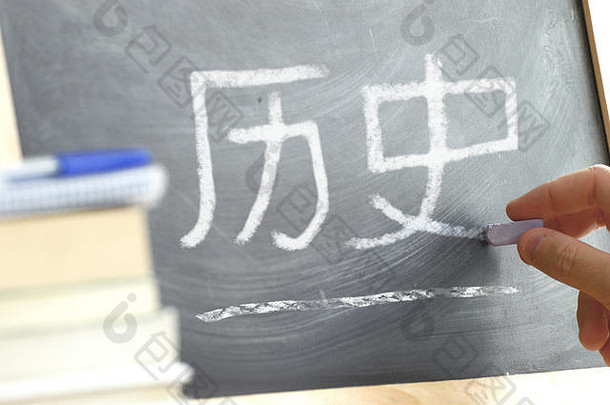 在中国历史课上，用手在黑板上写上“历史”一词。一些书和教材。