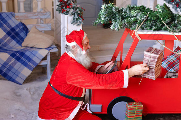 圣诞老人检查平板电脑上的礼物清单并放置礼物