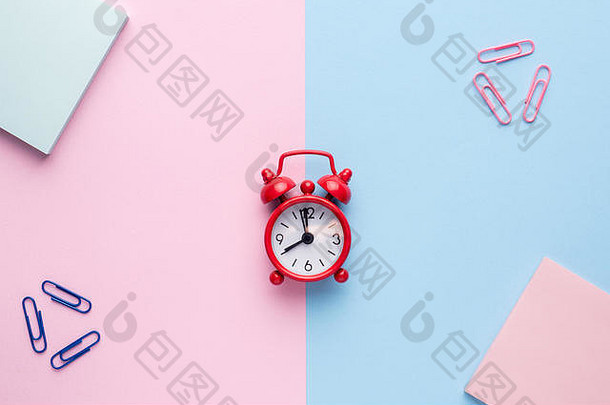 平铺在粉彩粉色和蓝色背景上，带有一个记事本回形针红色闹钟。