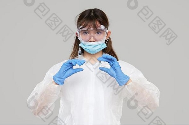 生物危害。中国冠状病毒的流行。一名身穿防护服和面具的亚洲妇女手持注射器和疫苗。疫苗f