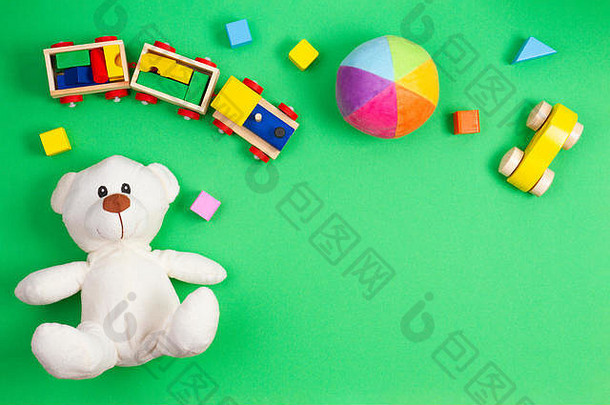 婴儿玩具背景。白色泰迪熊、木制玩具火车、汽车和绿色背景上的彩色积木。俯视图，平面布置