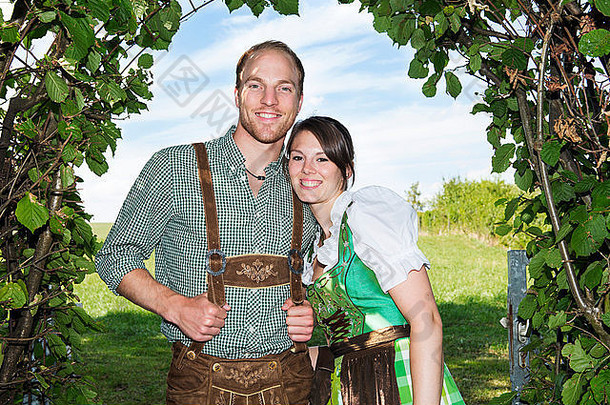 夫妇传统的巴伐利亚衣服站下面树