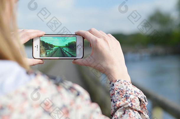 肩膀拍摄女人采取照片阳光明媚的河畔场景智能手机