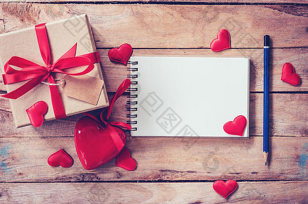 空白笔记本和礼品盒，木质背景上有红色心形图案。