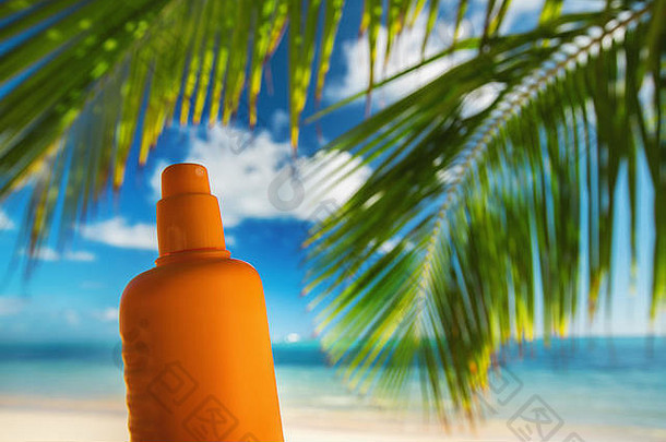 热带海滩上的一瓶防晒乳液和棕榈叶
