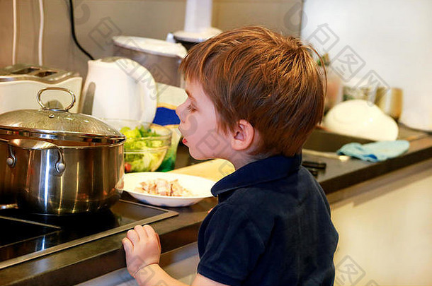 厨房里孩子的画像。可爱的小男孩，在厨房里玩耍。小孩饿了，看了看，检查午饭是否吃完了。童年，食物。