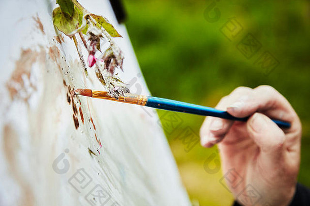 关闭艺术家应用油漆纸刷用钉子钉上植物材料艺术作品