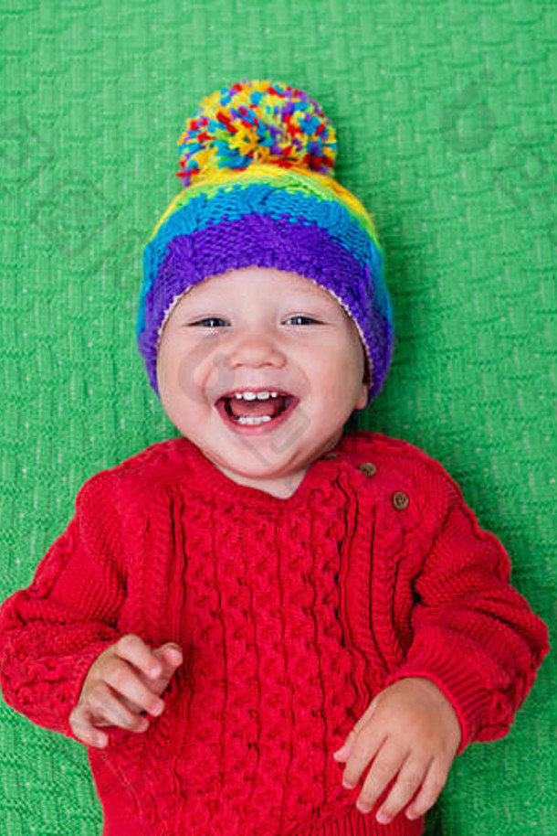 可爱的婴儿戴着温暖的羊毛针织帽，戴着红色毯子。儿童秋<strong>冬服装</strong>。彩色儿童针织品。