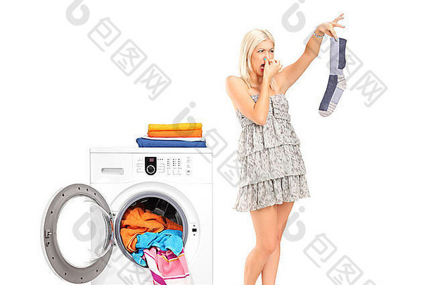 一位家庭主妇拿着一只<strong>男袜</strong>子，鼻子挨着一台被隔离在白色地板上的洗衣机
