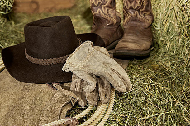 西部牛仔帽，牛仔靴，皮手套，皮套和谷仓里干草上的绳索