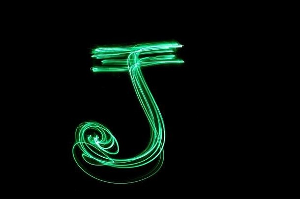 绿色灯光绘画摄影——黑色背景上字母系列的字母J。长曝光摄影，抽象绿色运动