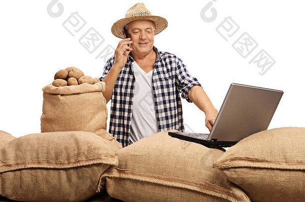 成熟的农民拿着装满土豆的麻袋摆好姿势，一边打电话，一边用笔记本电脑工作