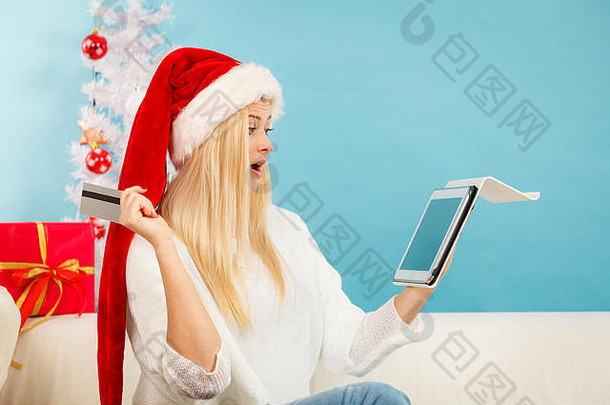 圣诞节时间概念。在家沙发上拿着平板电脑笔记本电脑和的年轻女孩在网上<strong>购物</strong>，购买礼物，