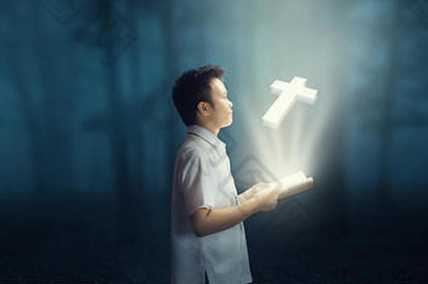 小男孩在黑暗的森林里<strong>读</strong>圣经。虚拟全息<strong>图</strong>十字架出自书中。美好的世界。