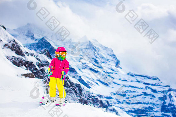 孩子们在山上滑雪。带安全帽、护目镜和杆子的活泼幼儿。幼儿滑雪比赛。冬季运动