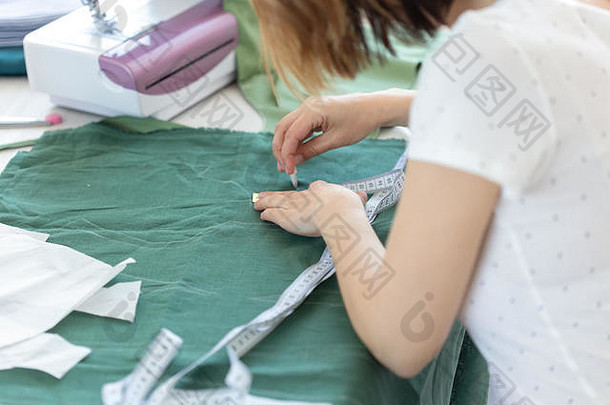 一位年轻女设计师的手在缝纫机旁边的桌子上为一种新的缝纫产品做标记。创意商业的概念与发展