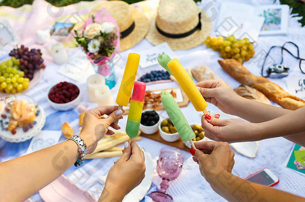 在夏日野餐的背景下，女人手拿着五颜六色的冰激凌棒。夏季周末。