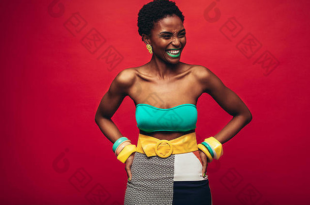 穿着时髦服装站在<strong>红色背景</strong>上的非洲女人。非洲女时装模特站在工作室里，<strong>双</strong>手放在臀部，面带微笑。