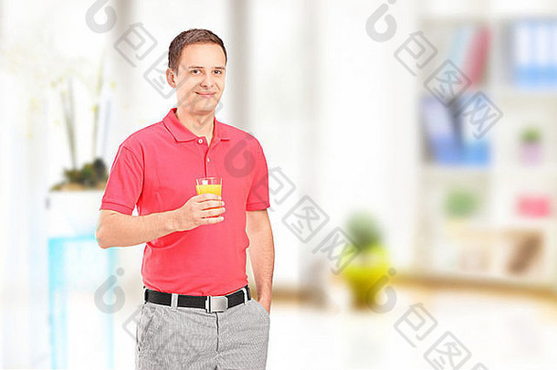 微笑的年轻人拿着一杯橙汁在家摆姿势