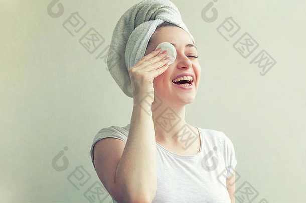 面带微笑的女人的美丽肖像，头戴毛巾，皮肤柔软健康，用白色背景上隔离的化妆棉<strong>卸妆</strong>。护肤洁面spa放松概念