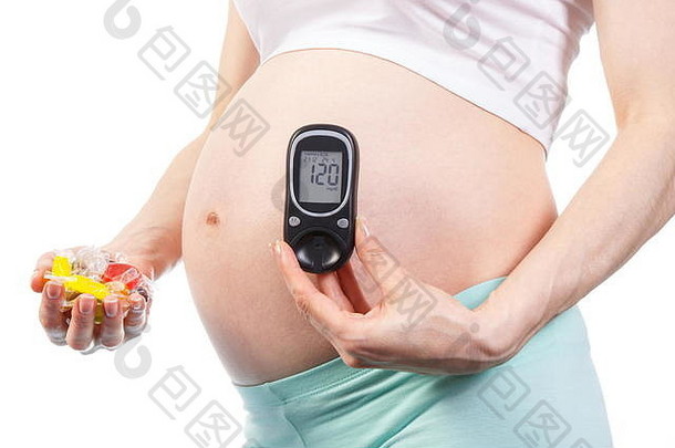 孕妇手持彩色糖果和血糖仪，测量血糖水平，减少吃糖和糖尿病的概念