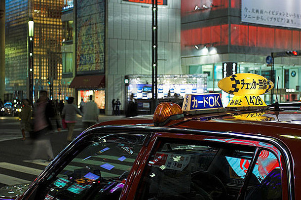 东京新宿，前景车，明亮的广告灯照亮背景，模糊的行人穿过马路。