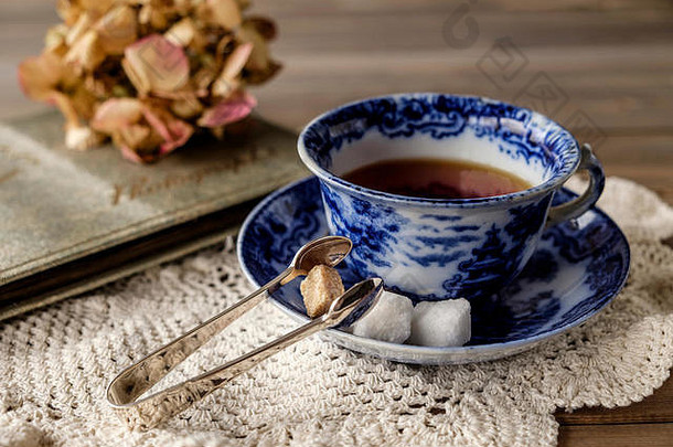 木制桌子上的古董青花瓷茶杯和茶托的特写镜头，茶杯和茶托的花边布上有褪色的花