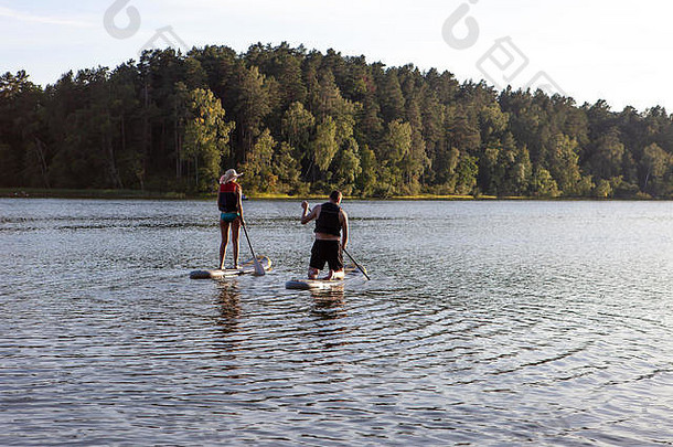 在一个安静的湖面上，用温暖的夏日夕阳颜色，站起来划桨冲浪