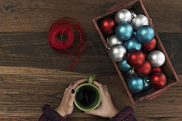 蓝色、红色、银色的装饰品和红色丝带放在木板上的盒子里一只手蜷缩在一杯咖啡周围休息