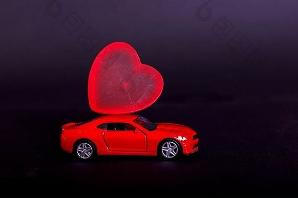 黑色背景上的情人节，黑色表面上印有心形图案的微型红色玩具车。文本的空白位置。