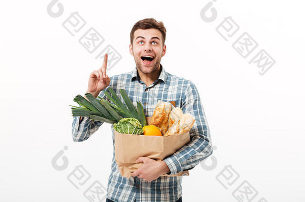 一个快乐的男人拿着装满食品的纸袋，在白色背景上孤立地竖起手指的肖像