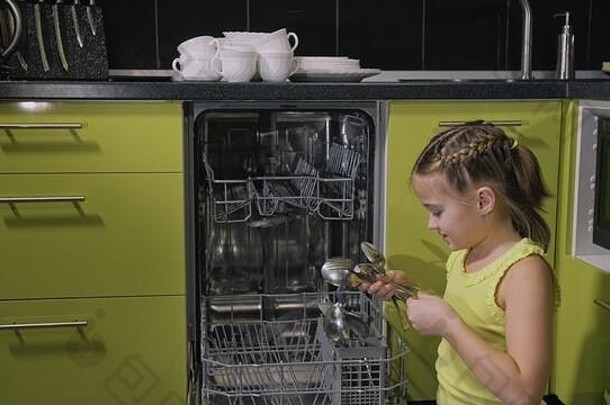 聪明的女孩正在学习使用洗碗机。绿色黑色的时尚现代内置厨房电器。孩子正在放脏盘子。