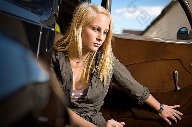 美丽的年轻金发女孩与黑色复古汽车合影。