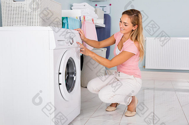 年轻快乐的女人在<strong>杂物间</strong>里使用洗衣机