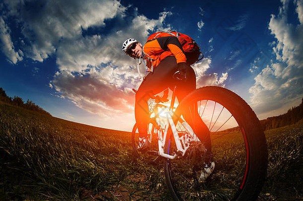 穿着橙色运动衫的骑自行车的人骑在绿色的夏季田野上
