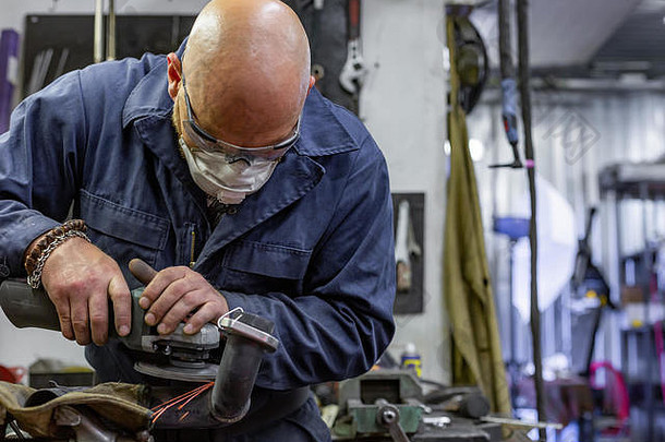 重型工业工人在汽车维修厂用角磨机切割钢材。
