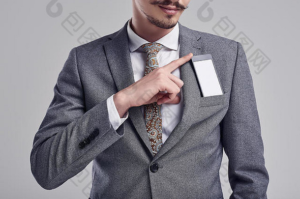 在studi上，一位英俊、自信的年轻阿拉伯商人的特写照片，他留着花哨的胡子，穿着时尚的灰色套装，将手机藏在口袋里