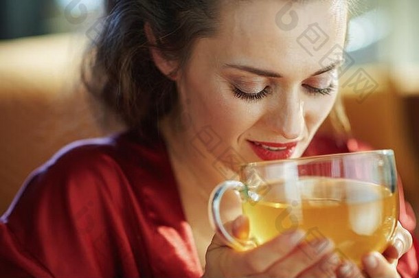 阳光明媚的现代客厅里，穿着黑色紧身内衣和红色浴袍，喝着一杯绿茶的中年妇女的肖像。