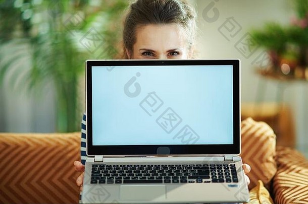 时尚的中间年龄女人蓝色的上衣条纹夹克现代首页阳光明媚的一天坐着沙发上显示移动PC空白屏幕