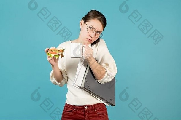 心怀不满的女孩拿着咖啡、文件和电话，试图吃三明治。蓝色背景