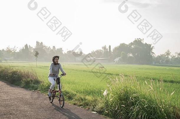 年轻妇女戴着头盔在稻田里骑折叠自行车