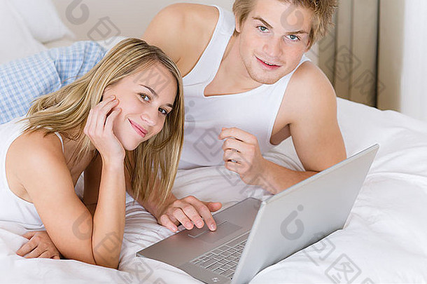 这对年轻夫妇躺在床上休息，笔记本电脑一起躺着