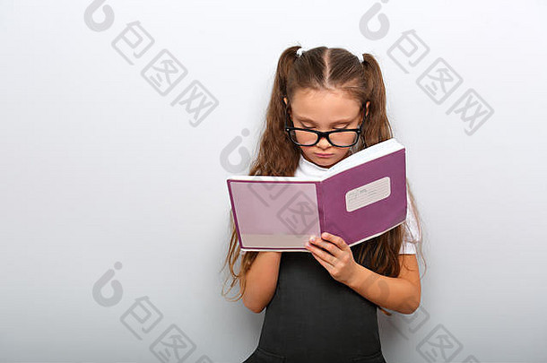聪明的小学生戴眼镜的小女孩看着课本，在蓝色背景上做练习