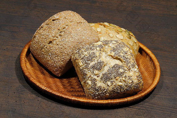 各种类型的面包卷、蛋糕、小面包，放在一个篮子里，放在一个质朴的木制表面上
